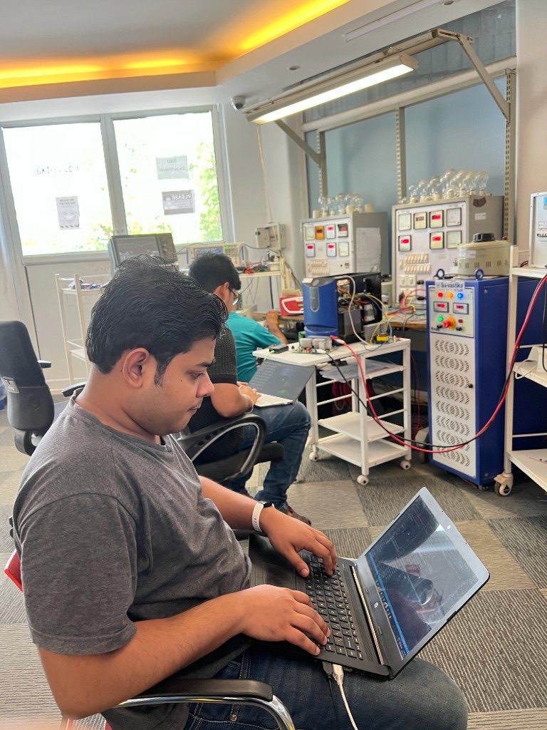 Engineers at laptops on a crowded Indian MSME power-electronics shop floor with test racks and load banks
