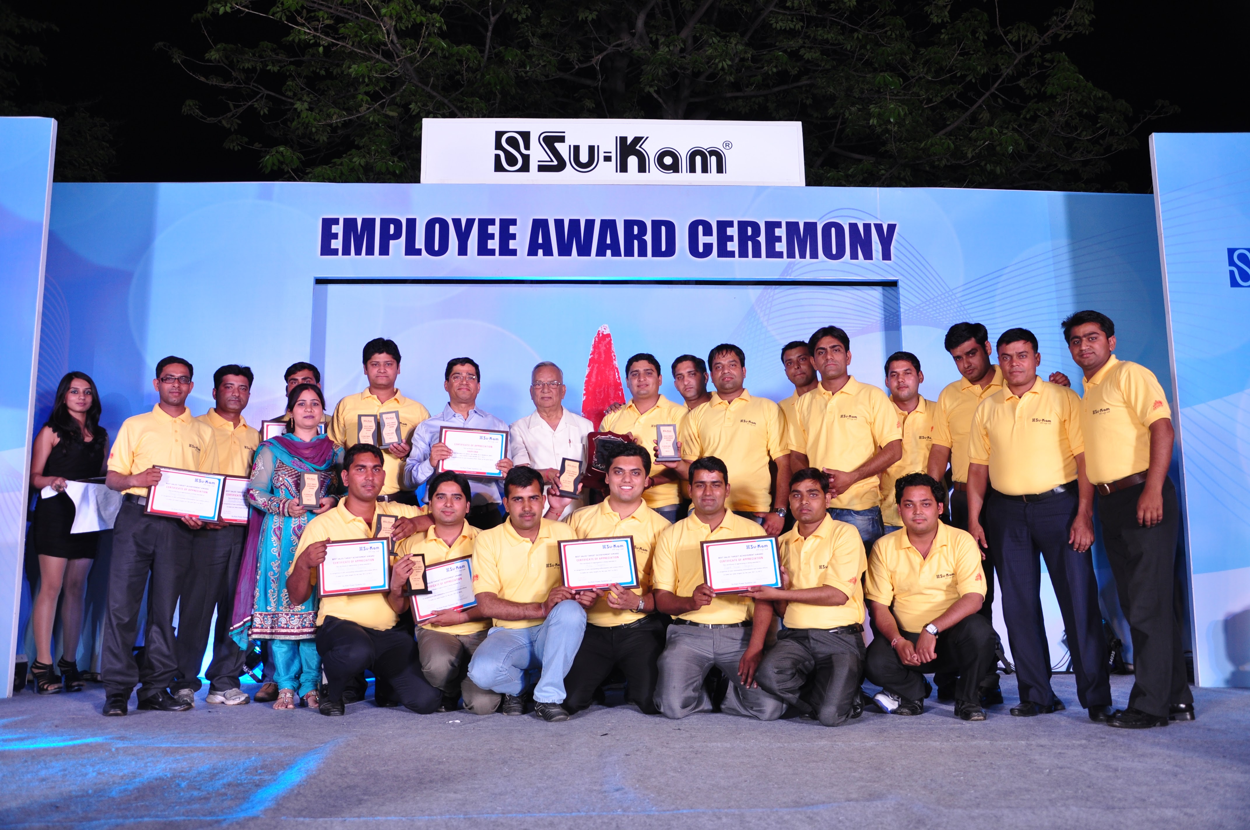 Su-Kam employees receiving awards on stage under the company logo